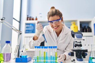 Laboratuvarda pipet kullanan bilim adamı üniforması giyen genç sarışın kadın.