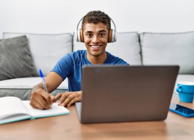 Genç İspanyol adam evde dizüstü bilgisayarla ders çalışıyor.