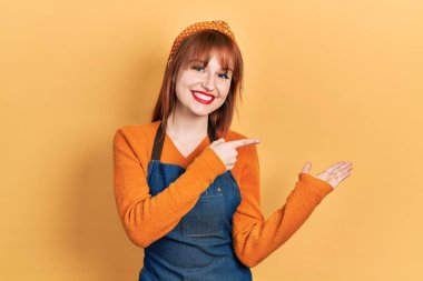 Kızıl saçlı, önlük giymiş genç bir kadın kameraya hayret ediyor ve gülümsüyor.. 