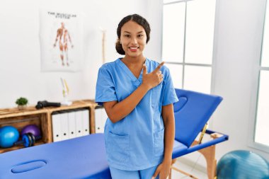 Güzel İspanyol fizyoterapist kadın, acılı tedavi kliniğinde mutlu, yüzünde mutlu ve doğal bir ifadeyle, elleri ve parmaklarıyla yüzünü gösteren bir gülümseme ile. 