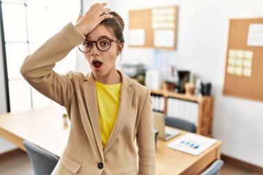 Young brunette teenager wearing business style at office surprised with hand on head for mistake, remember error. forgot, bad memory concept. 