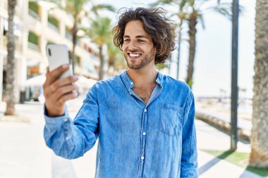 Genç İspanyol adam şehrin caddesinde yürürken akıllı telefondan selfie çekiyor..