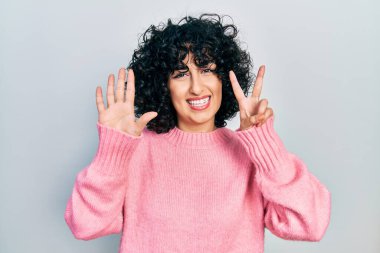 Orta Doğulu genç bir kadın günlük kıyafetler giyer ve yedinci parmaklarını göstererek gülümseyerek mutlu ve kendinden emin bir şekilde gösterir.. 