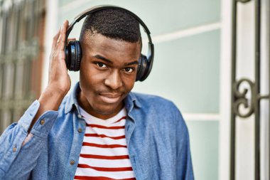 Young african american man with serious expression using headphones at the city.