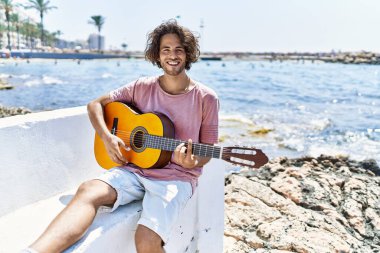 Genç İspanyol adam klasik gitar çalıyor sahildeki bankta oturuyor..