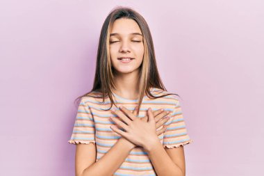 Young brunette girl wearing casual striped t shirt smiling with hands on chest, eyes closed with grateful gesture on face. health concept. 