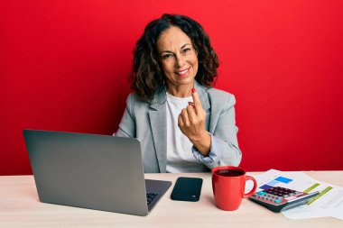 Beautiful middle age woman working at the office drinking a cup of coffee beckoning come here gesture with hand inviting welcoming happy and smiling 