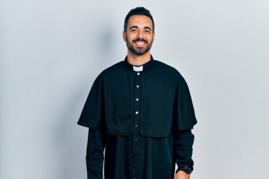 Handsome hispanic man with beard wearing catholic priest robe with a happy and cool smile on face. lucky person. 