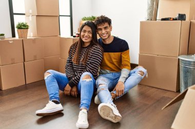 Young latin couple smiling happy sitting on the floor at new home.