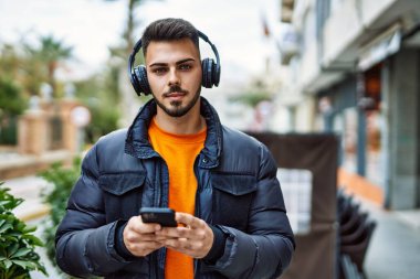 Yakışıklı, sakallı, mutlu ve kendine güvenen, akıllı telefon kullanan, kışlık palto giyen bir İspanyol.