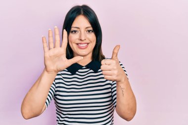 Genç İspanyol kadın gündelik giysiler giyiyor. Altıncı parmaklarını gösterip işaret ederken kendinden emin ve mutlu bir şekilde gülümsüyor.. 