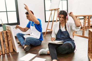 Sanat okulunda iki öğrenci kulaklık takıp resim yaparken mutlu bir şekilde gülümsüyor..
