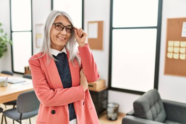 Orta yaşlı, kır saçlı, iş kadını. Ofiste kendinden emin bir şekilde gülümsüyor.
