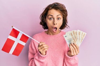 Elinde Norveç bayrağı ve Krone banknotları tutan genç esmer kadın şaşkınlık ve şaşkınlık içinde bir ifade, korku ve heyecan dolu bir yüz vardı.. 