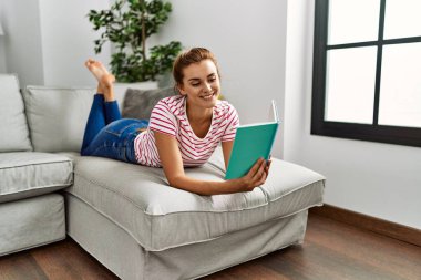 Evdeki kanepede kitap okuyan genç bir kadın.