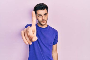 Gündelik tişört giyen genç İspanyol adam parmağını kaldırmış ve kızgın bir ifadeyle işaret ediyor. Hiç hareket göstermiyor. 