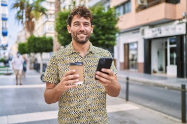 Genç İspanyol adam akıllı telefon kullanıyor, sokakta kahve içiyor.