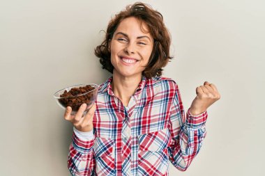 Kuru üzümlü kase tutan genç esmer kadın gururla haykırıyor zaferi ve başarıyı kutluyor. 