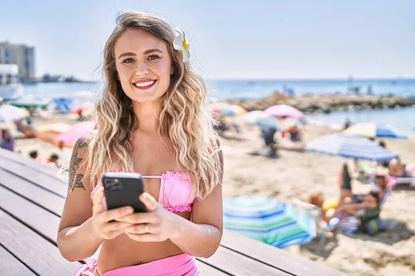 若いですブロンド女の子使用してスマートフォン座っていますザベンチにザビーチ — ストック写真