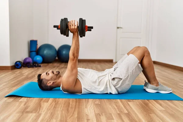 Joven Hispano Sonriendo Confiado Entrenamiento Usando Mancuernas Centro Deportivo —  Fotos de Stock