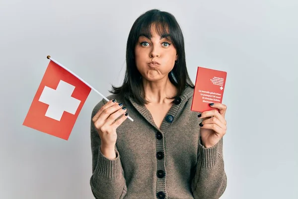 Young Hispanic Woman Holding Swiss Flag Passport Puffing Cheeks Funny — Fotografia de Stock