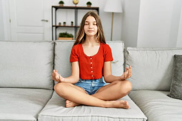 可爱的女孩坐在家里的沙发上做瑜伽练习 — 图库照片
