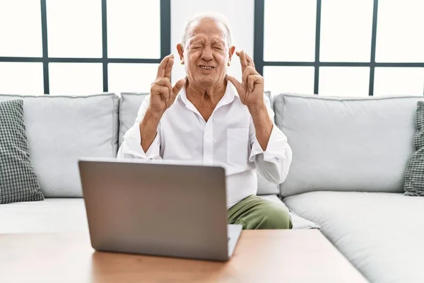 Senior Man Using Laptop Home Sitting Sofa Gesturing Finger Crossed —  Fotos de Stock