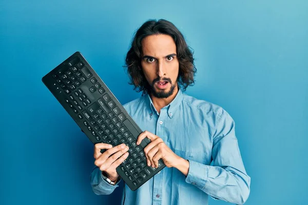 Young Hispanic Man Holding Keyboard Shock Face Looking Skeptical Sarcastic — Stock fotografie