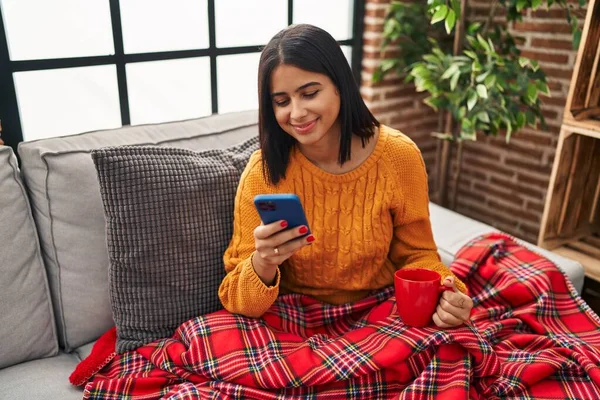 若いラテン語の女性はコーヒーを飲み 自宅でスマートフォンを使用して — ストック写真