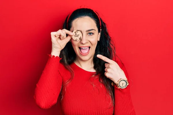 Young Hispanic Woman Holding Cookie Eye Smiling Happy Pointing Hand — Stockfoto