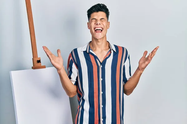 Young Hispanic Man Standing Close Empty Canvas Celebrating Mad Crazy — Stockfoto