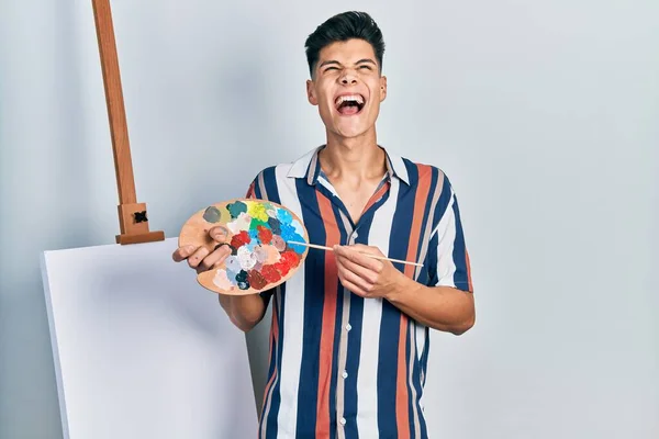 Young Hispanic Man Holding Painter Palette Paintbrush Standing Close Canvas —  Fotos de Stock