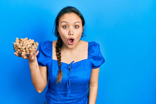 Young Hispanic Girl Holding Bowl Peanuts Scared Amazed Open Mouth — Stockfoto