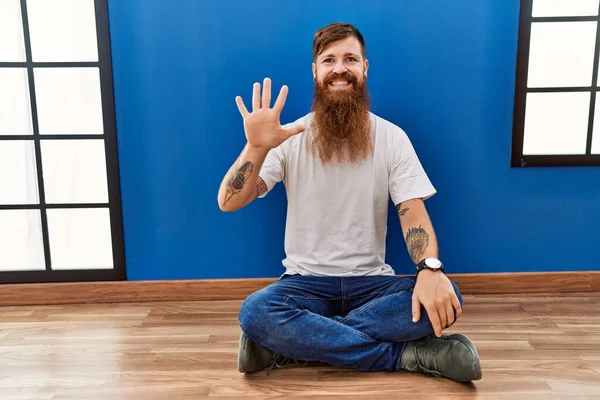 Redhead Man Long Beard Sitting Floor Empty Room Showing Pointing — Stockfoto