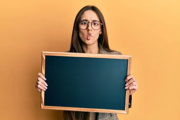 Young Hispanic Girl Holding Blackboard Making Fish Face Mouth Squinting — Stock Photo, Image