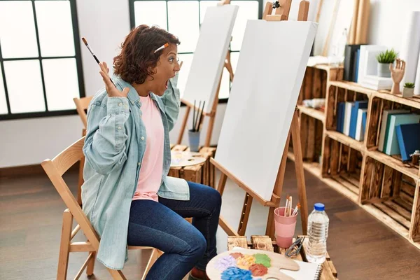 Sanat stüdyosunda resim yapan orta yaşlı bir kadın zaferi mutlu bir gülümseme ve ellerini kaldırarak kazanan bir ifadeyle kutluyor. 