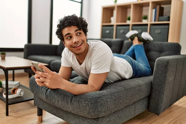 Ung Latinamerikan Man Med Smartphone Liggande Soffan Hemma — Stockfoto