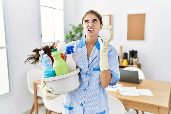Young Blonde Woman Wearing Cleaner Uniform Holding Cleaning Products Crazy — стоковое фото