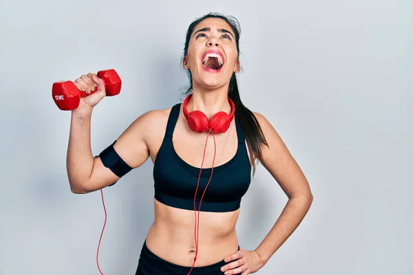 Young Hispanic Girl Wearing Sportswear Using Dumbbell Angry Mad Screaming — Stockfoto
