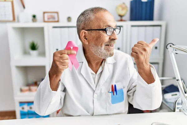Mature Doctor Man Holding Pink Cancer Ribbon Clinic Pointing Thumb — Foto Stock