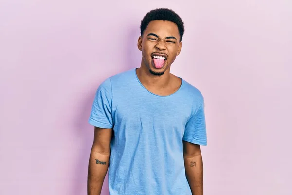カジュアルなブルーのTシャツを着た若いアフリカ系アメリカ人男性が面白い表情で幸せ舌を突き出しています 感情の概念 — ストック写真