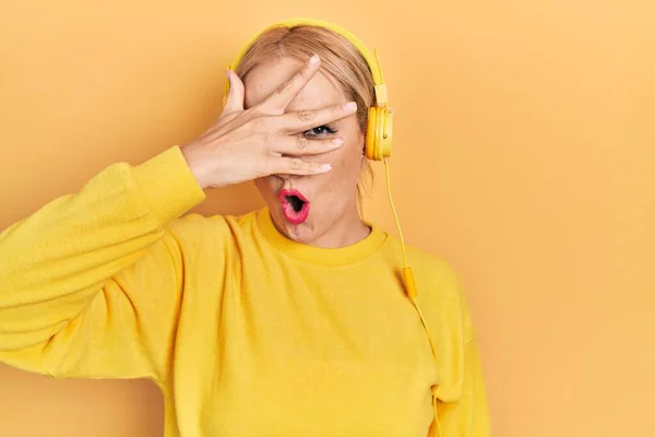 Young Blonde Woman Listening Music Using Headphones Peeking Shock Covering — Stok fotoğraf