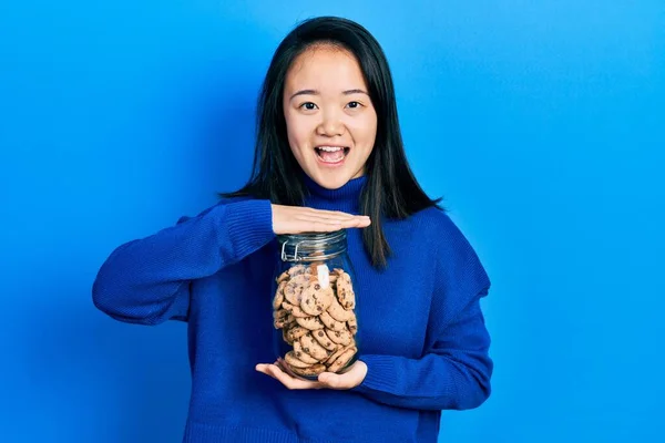 Young Chinese Girl Holding Jar Chocolate Chips Cookies Celebrating Crazy — Stockfoto