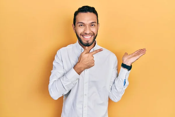 ビジネスシャツを着て髭を生やしたヒスパニック系の男は驚いて 手で提示しながら カメラに笑みを浮かべて指で指して — ストック写真