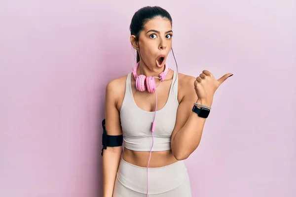 Young Hispanic Woman Wearing Gym Clothes Using Headphones Surprised Pointing — Fotografia de Stock