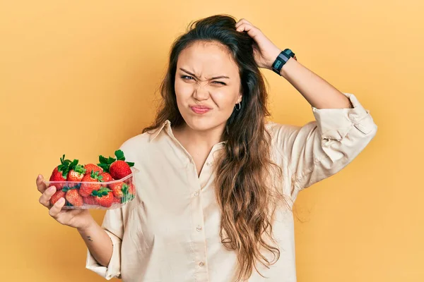 Young Hispanic Girl Holding Strawberries Confuse Wondering Question Uncertain Doubt — Foto de Stock
