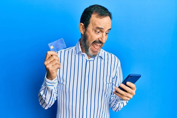 Middle Age Hispanic Man Using Smartphone Holding Credit Card Celebrating — Zdjęcie stockowe