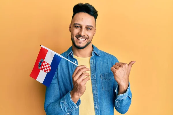 Young Arab Man Holding Croatia Flag Pointing Thumb Side Smiling — Stok fotoğraf