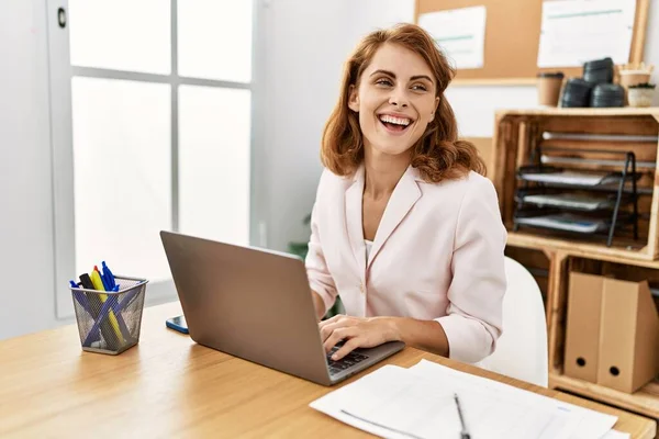 年轻的高加索女商人在办公室用笔记本电脑开心地微笑着 — 图库照片