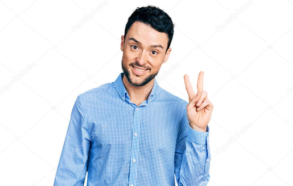 Hispanic man with beard wearing casual business shirt smiling with happy face winking at the camera doing victory sign. number two. 